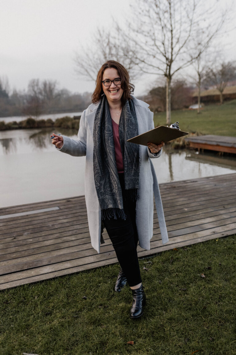 fröhliche Hochzeitsplanerin am Steg vor einem Weiher mit Checkliste bei der Locationbesichtigung für ein Hochzeitspaar Eventlocation finden Augsburg Bayreuth Bamberg Ingolstadt Nürnberg
