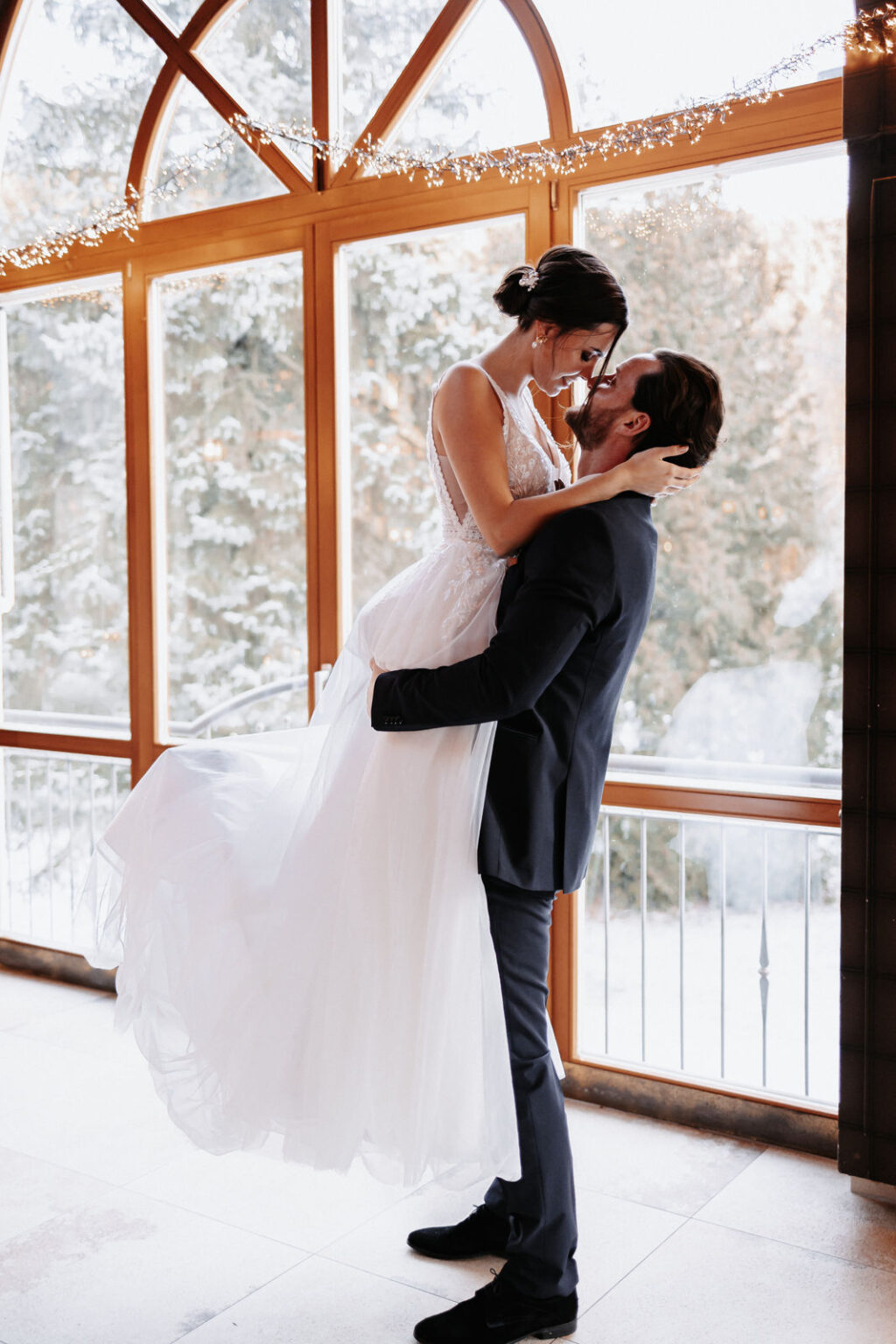 Bräutigam-hebt-seine-Braut-hoch-vor-wunderschönem-Fenster-Location-in-Mittelfranken-mit-Aussicht-Winterhochzeit-Hochzeitsplaner-Nürnberg